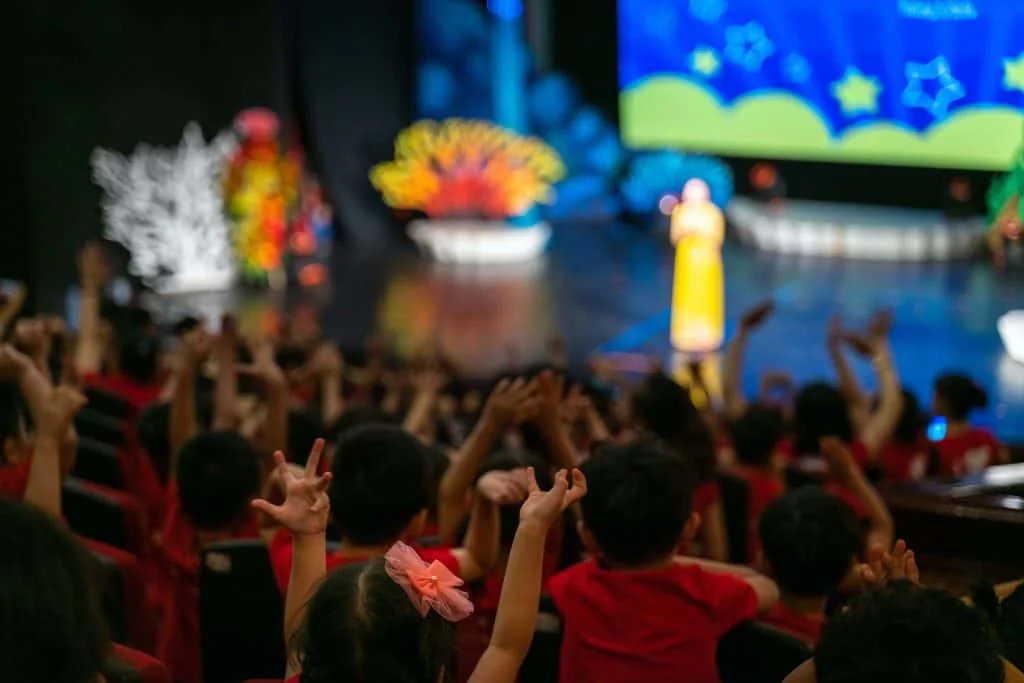 Children excitingly raise hands watching the performance in the theatre