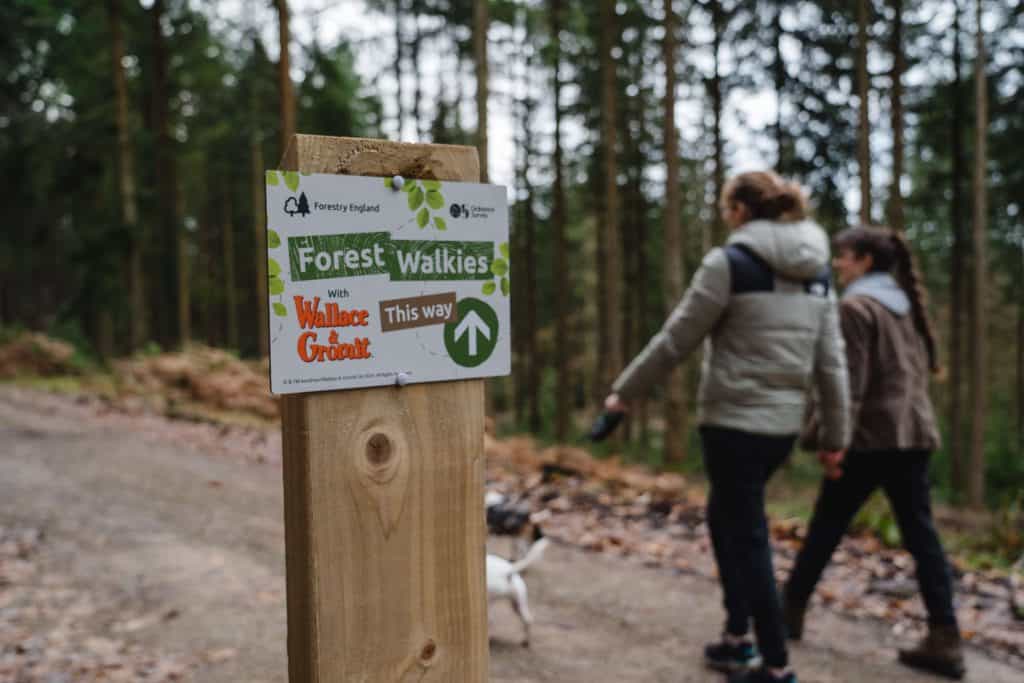 Two walkers pass a Forest Walkies trail sign in the forest