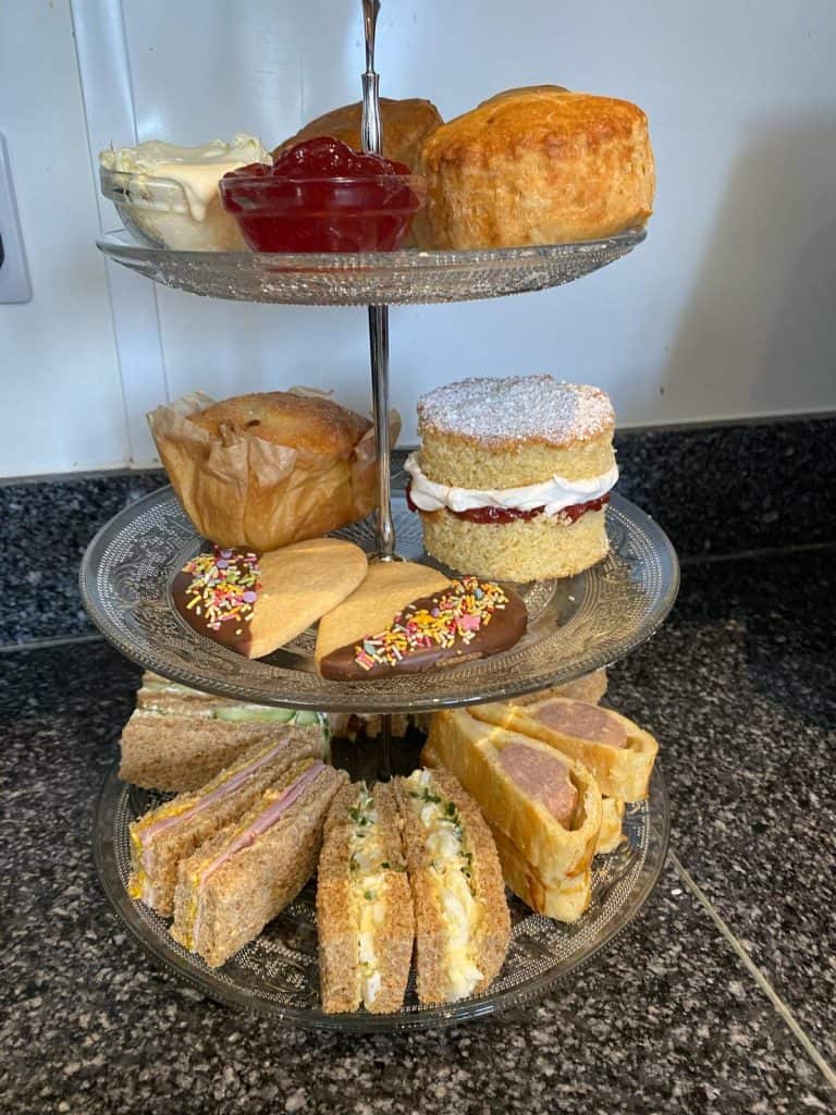 A three tier cake stand with afternoon tea including sandwiches and cakes