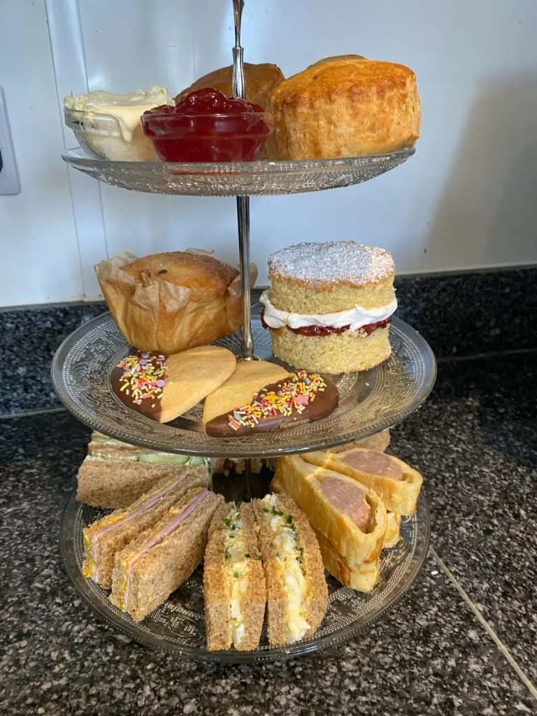 A three tier cake stand with afternoon tea including sandwiches and cakes