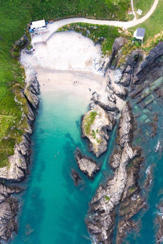 A view of the narrow Barricade Beach in Woolacombe from above. The sea is clear turquoise ad the beach is white sand