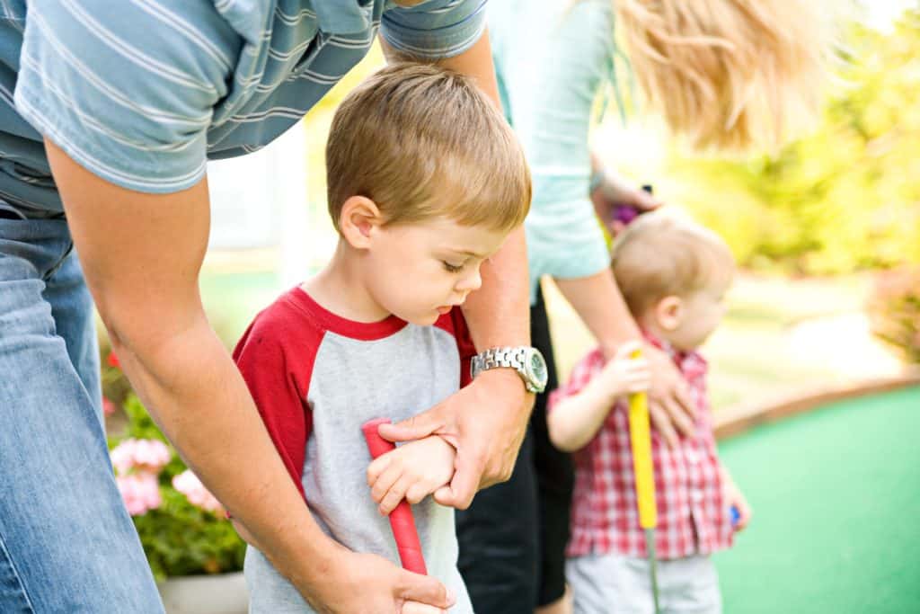 Two young children play mini golf with their parents
