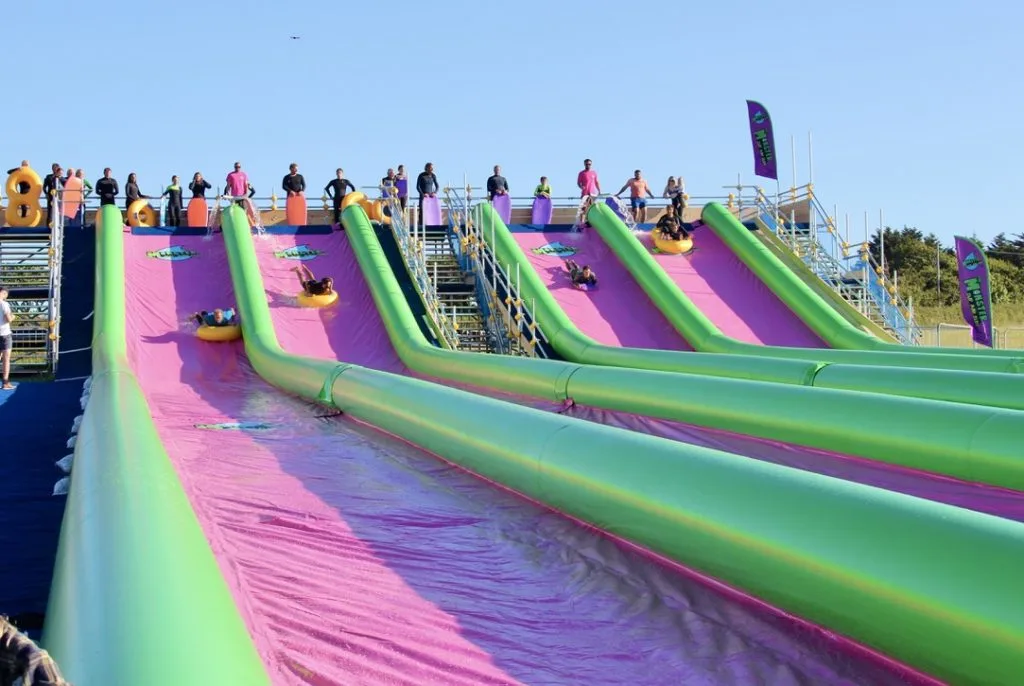 Photo of four purple and green slid and slide runs with people sliding down them on rubber rings