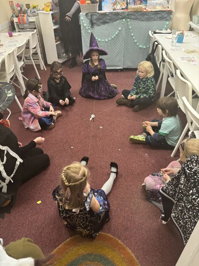 A circle of children dresses in Halloween outfits playing a game with string