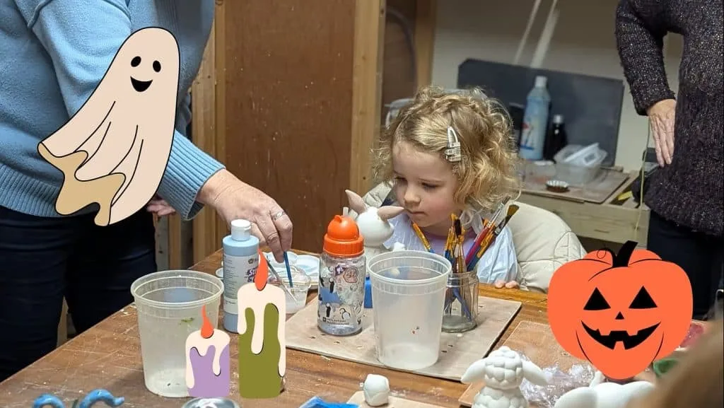 Child sat at crafting table painting pottery