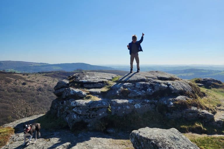 Child and dog on top of a Dartmoor tor on a bright sunny day