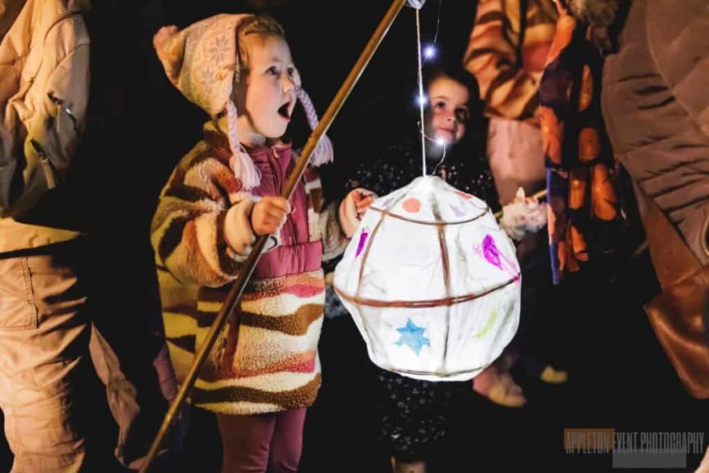 Child wrapped up on a winter night, holding a homemade paper lantern