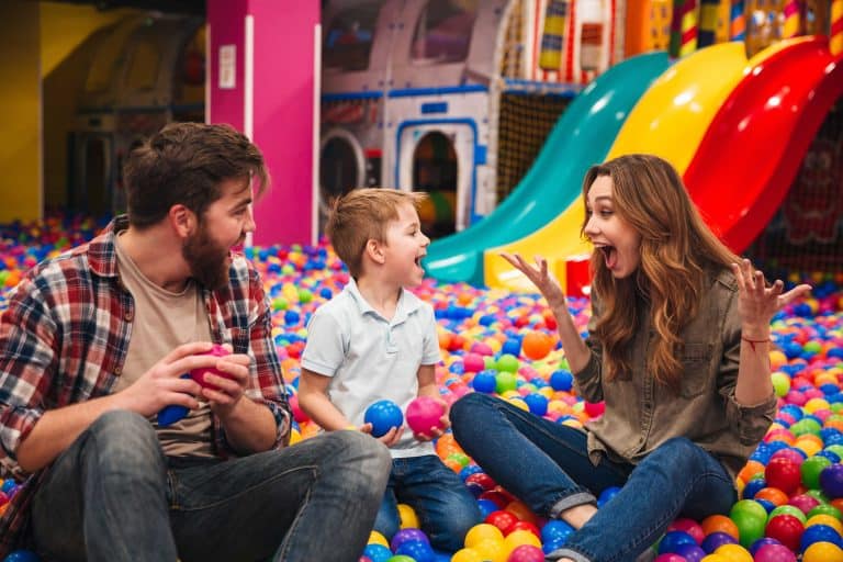 Young happy family with their little son spending time together in a soft play place