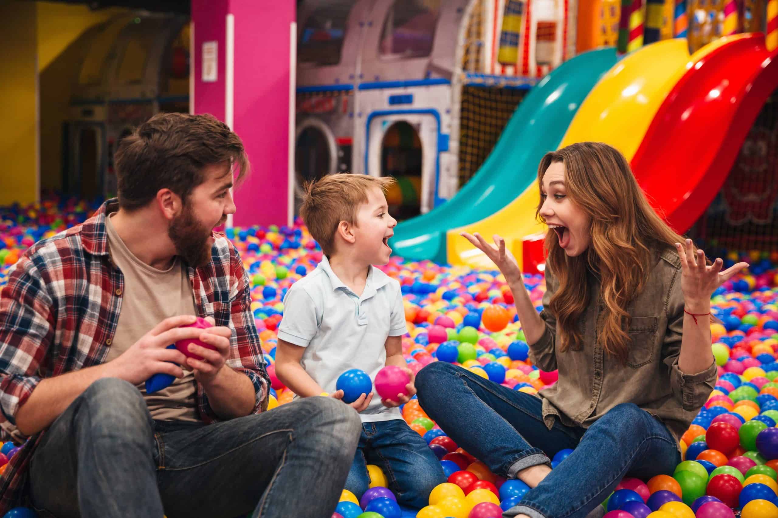 Young happy family with their little son spending time together in a soft play place