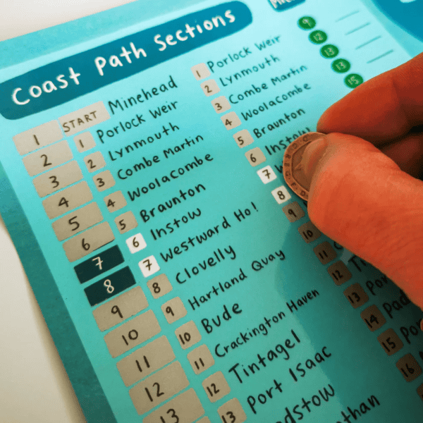 Hand with coin scratching locations on the South West Coast Path Scratch Off Map