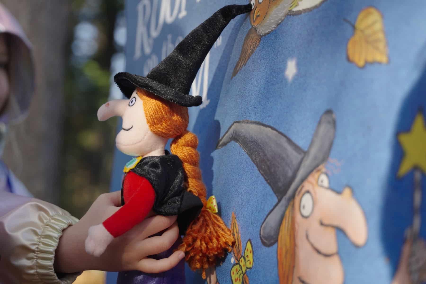 A toy witch from the Room on the Broom being help up to an activity board in the forest