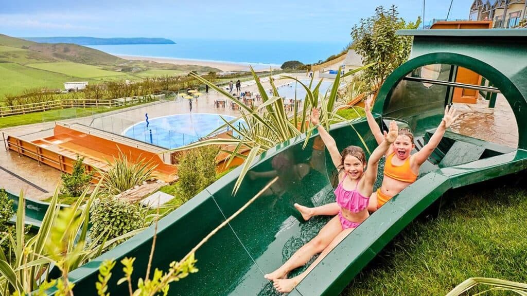 Children on a waterslide at Woolacombe Bay Holiday Park with the coast and beach in the background
