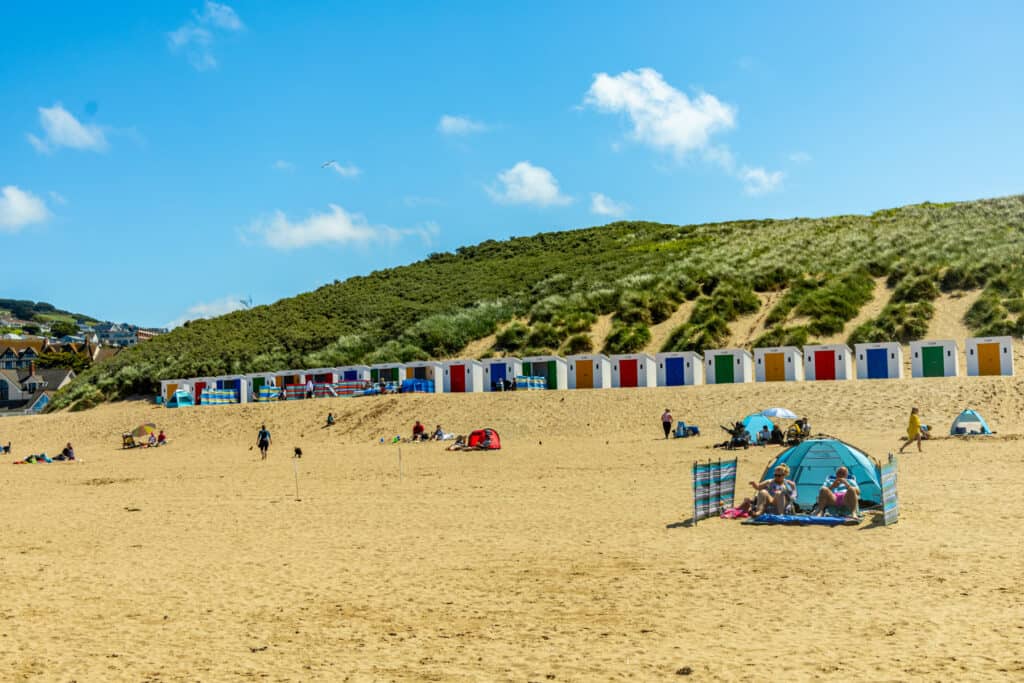 Holiday makers on Woolacombe beach with beach huts and sand dunes in the background