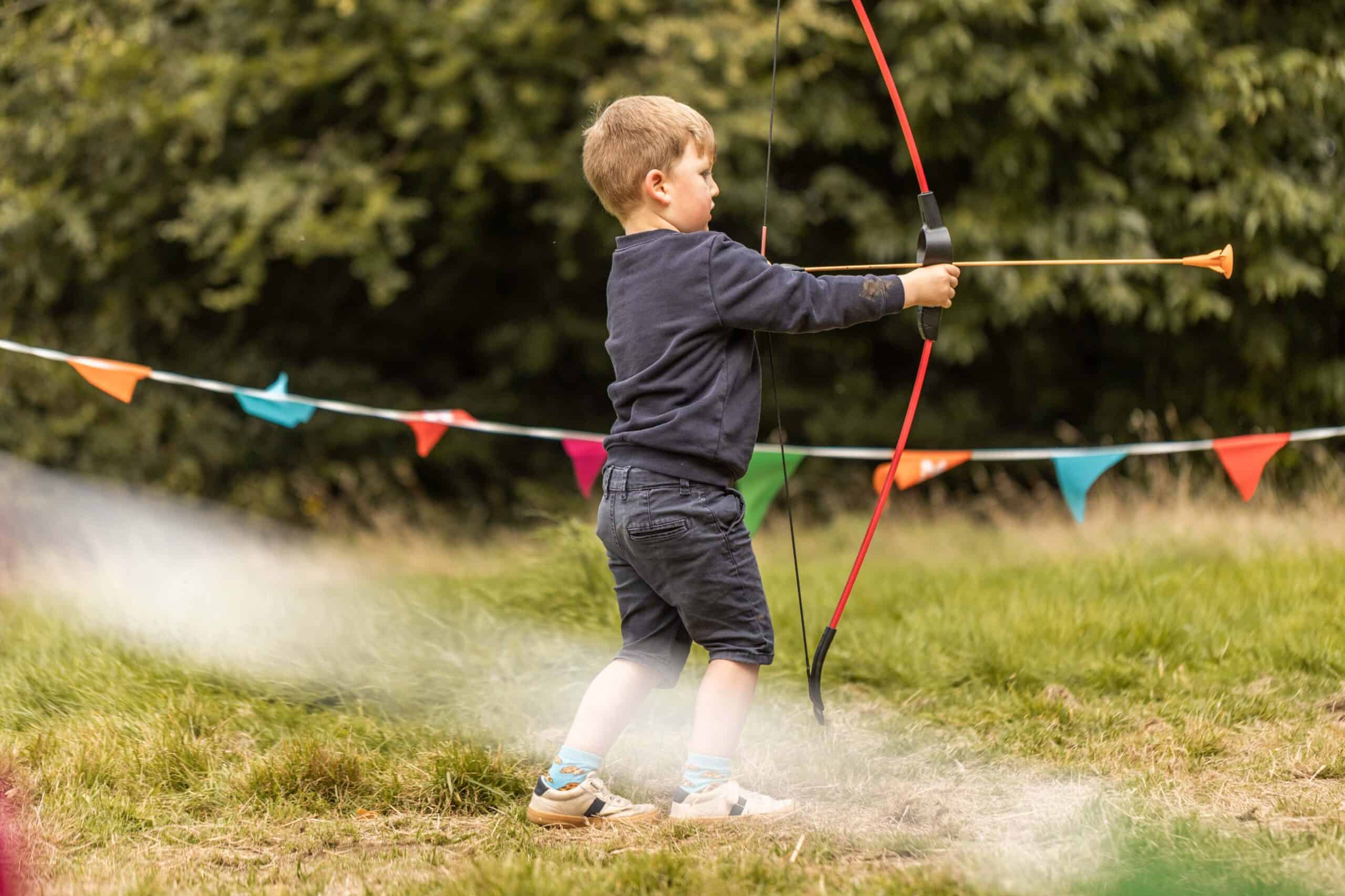 Young boy plays with a toy bow and arrow in a field at Arlington Court National Trust